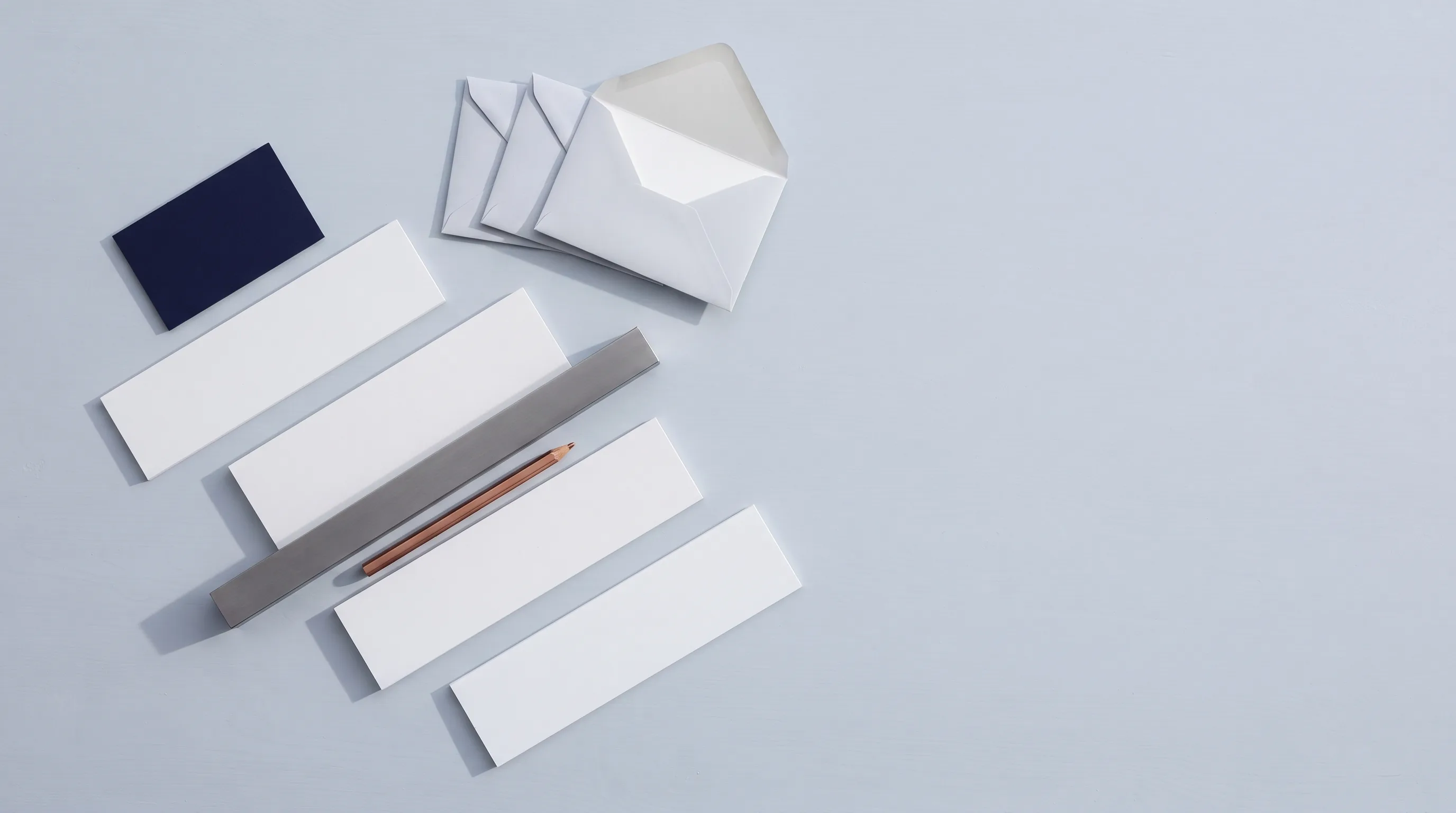 Cuatro tiras de papel escalonadas sujetas por una regla de acero, con un lápiz de cobre y cuatro sobres.